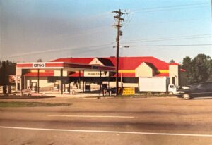 A Citgo gas station with a red roof, food court, several fuel pumps, and a white truck parked outside. A yellow sign reads 
