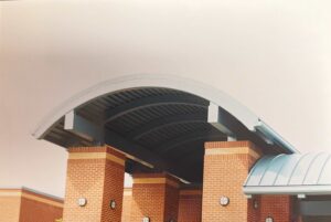 Curved metal roof supported by tall brick columns with round wall-mounted lights on a modern building.