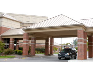 A black SUV is parked under the covered entrance of a brick building, possibly a hospital or medical facility, on a cloudy day.