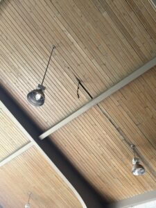 Wooden ceiling with two industrial light fixtures and a visible crack with exposed wires running along one of the wooden planks.