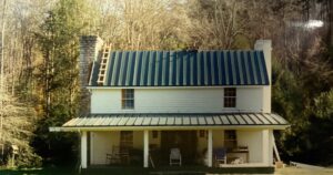 A two-story white house with a metal roof, a front porch with chairs, and a wooden ladder leaning against the roof, surrounded by trees.