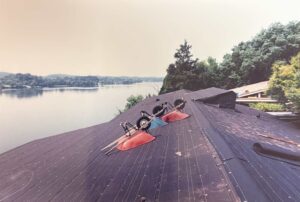A view of a lake from a rooftop under construction, with two wheelbarrows, tools, and trees in the background.