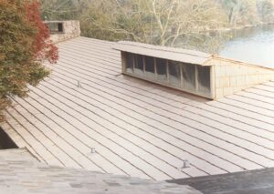 Flat roof with light-colored panels, featuring a rectangular rooftop structure with multiple windows; trees and water in the background.