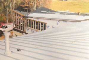 A partially constructed building with Tyvek-wrapped walls and a metal roof; construction materials and a red van are visible on site.