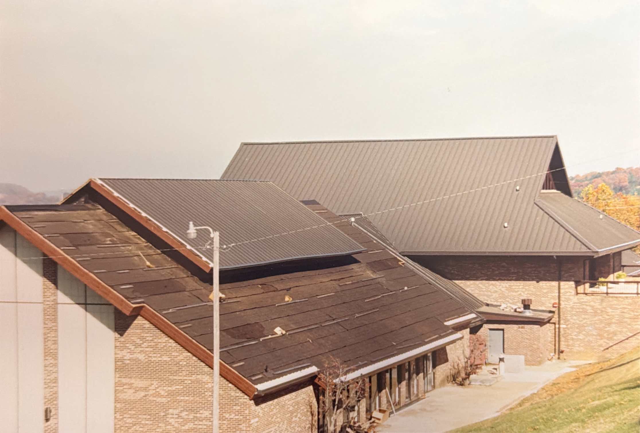 Several brick buildings with sloped, partially worn roofs are seen from above, set on a slight hill with a sidewalk and a lamppost in the foreground.