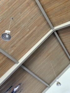 A wooden ceiling with white beams and two industrial-style hanging light fixtures.